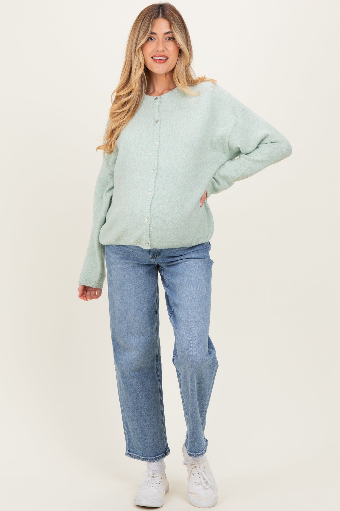 woman wearing a mint green maternity cardigan and light blue jeans, showing her baby bump