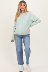woman wearing a mint green maternity cardigan and light blue jeans, showing her baby bump