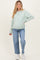 woman wearing a mint green maternity cardigan and light blue jeans, showing her baby bump