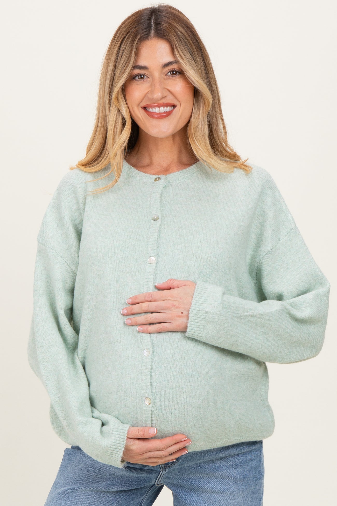 woman wearing a light green maternity cardigan with buttons, holding her baby bump