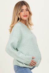 woman wearing a soft green maternity cardigan with buttons, gently cradling her baby bump
