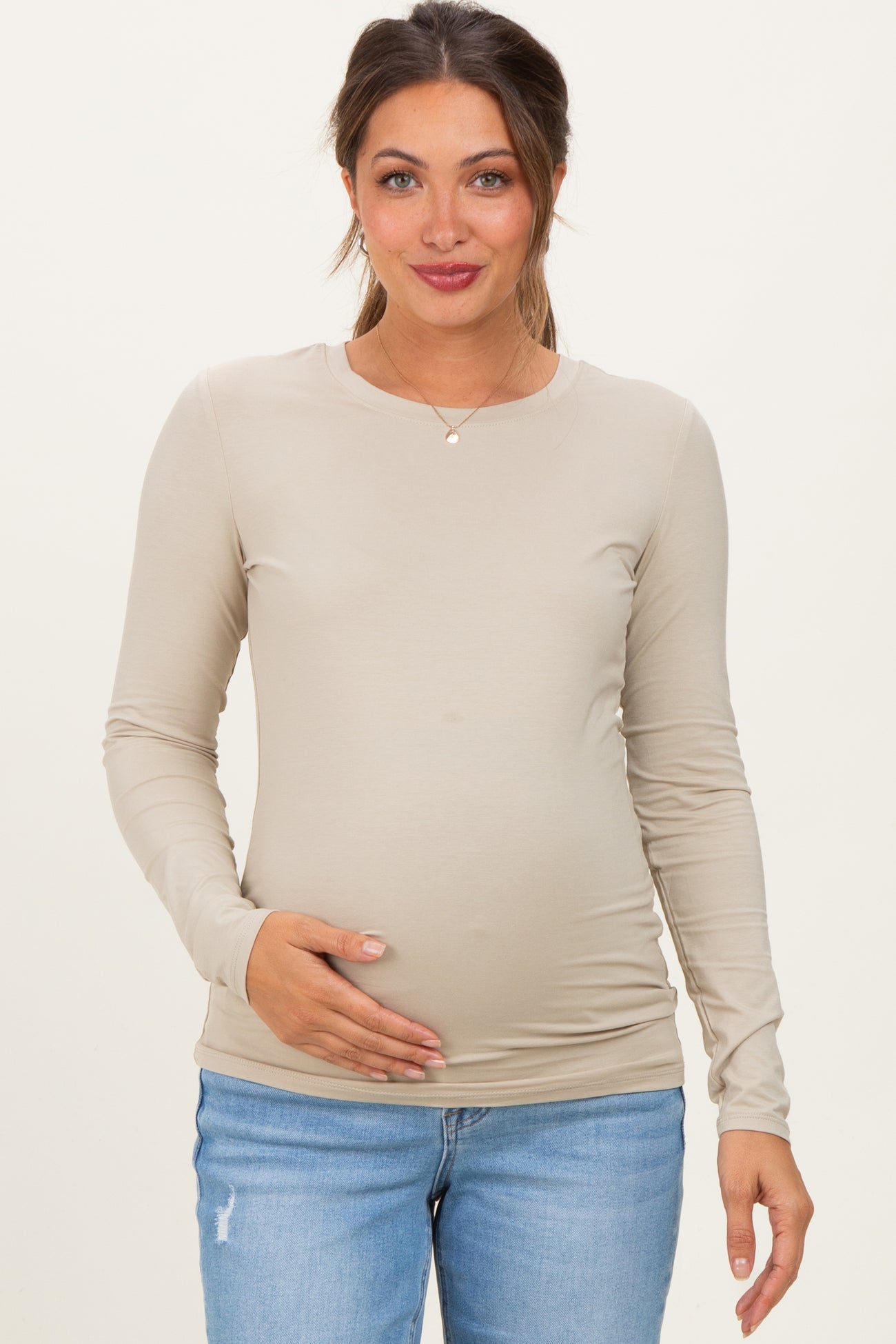 woman wearing a beige long sleeve maternity top and holding her baby bump