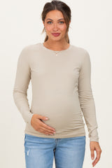 woman wearing a beige long sleeve maternity top and holding her baby bump
