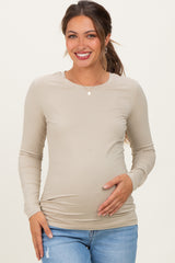 woman wearing a beige long sleeve maternity top and holding her baby bump