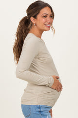 woman wearing a beige long sleeve maternity top and holding her baby bump