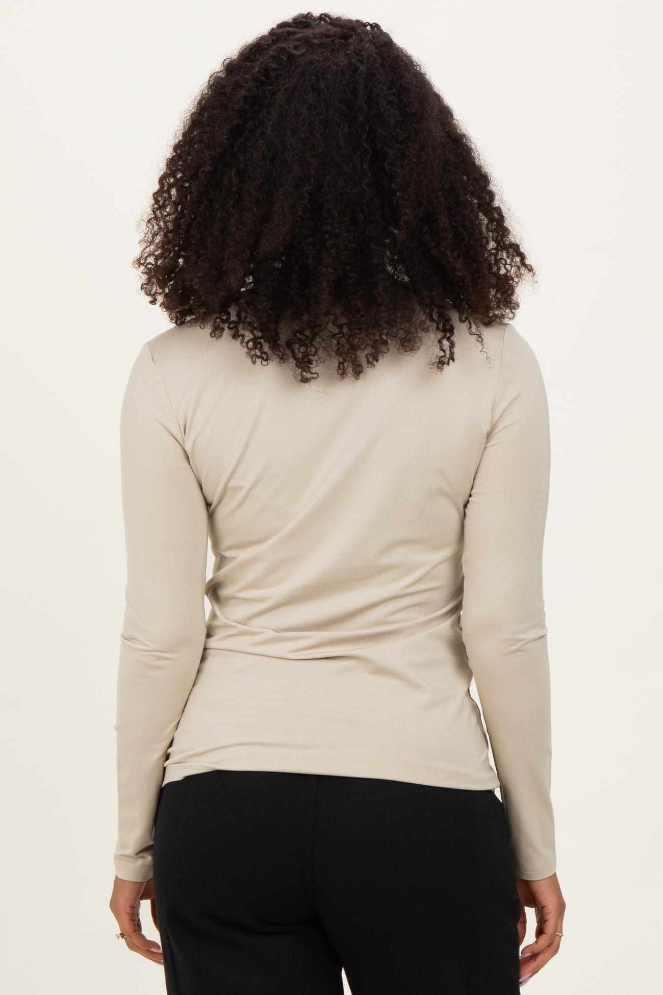 woman wearing a beige long sleeve top viewed from the back with curly hair