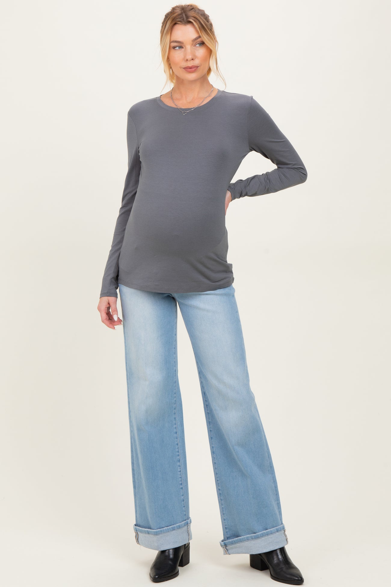 woman wearing a dark gray long sleeve maternity top and light blue wide-leg jeans with a visible baby bump