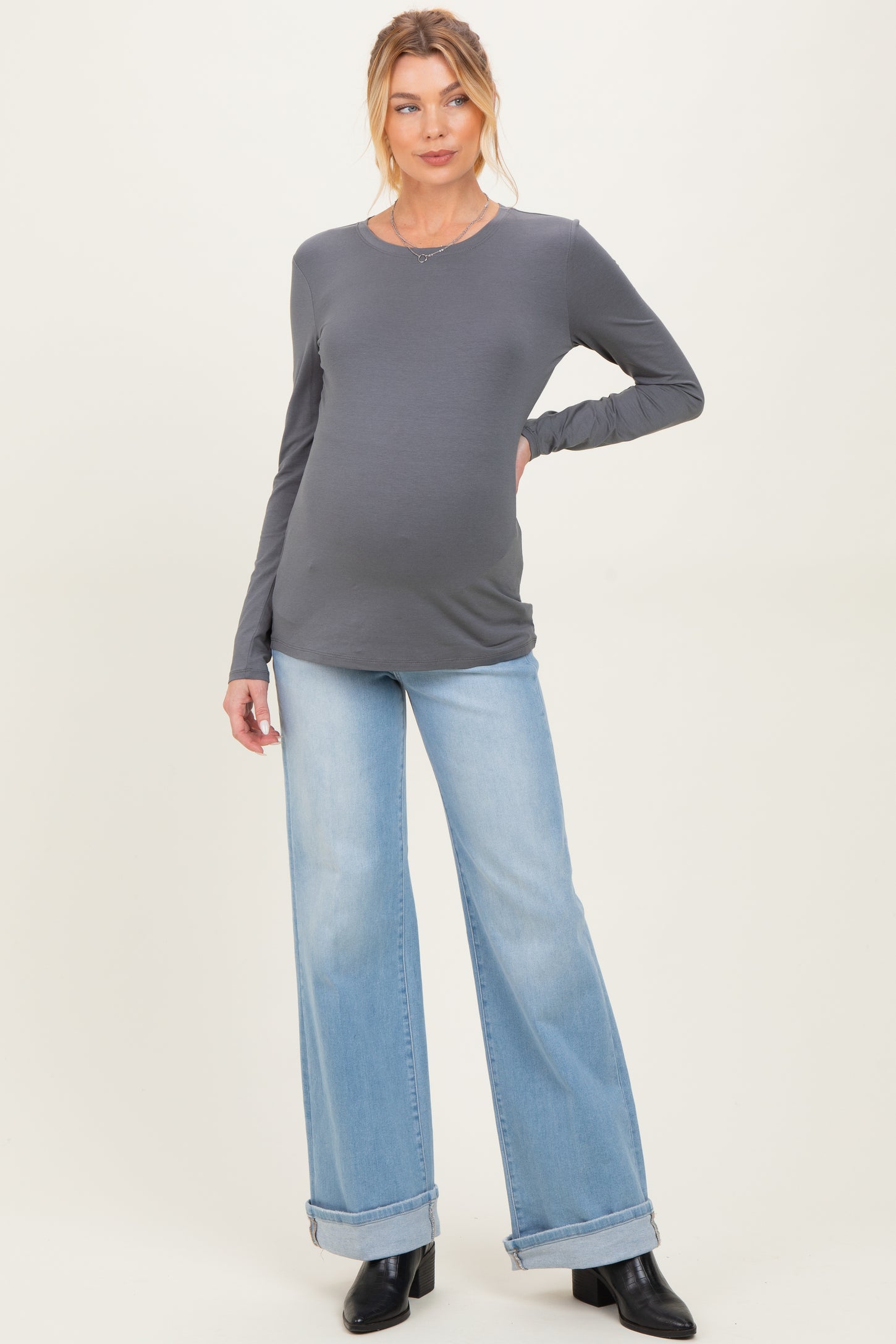 woman wearing a dark gray long sleeve maternity top and light blue wide-leg jeans with a visible baby bump