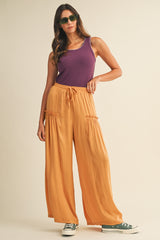 woman wearing a purple tank top and orange wide-leg pants, accessorized with green sunglasses and sneakers