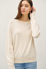 woman wearing a beige long sleeve sweater with a relaxed fit and round neckline, paired with light blue jeans