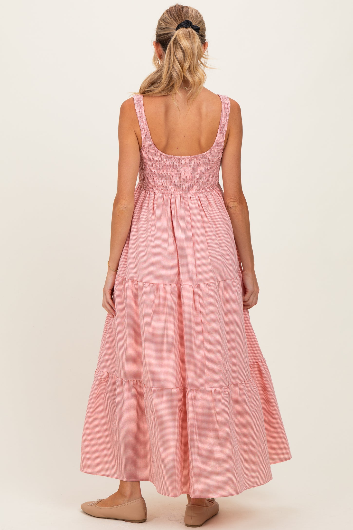 woman wearing a pink striped maternity maxi dress with a smocked bodice and tiered skirt, seen from the back