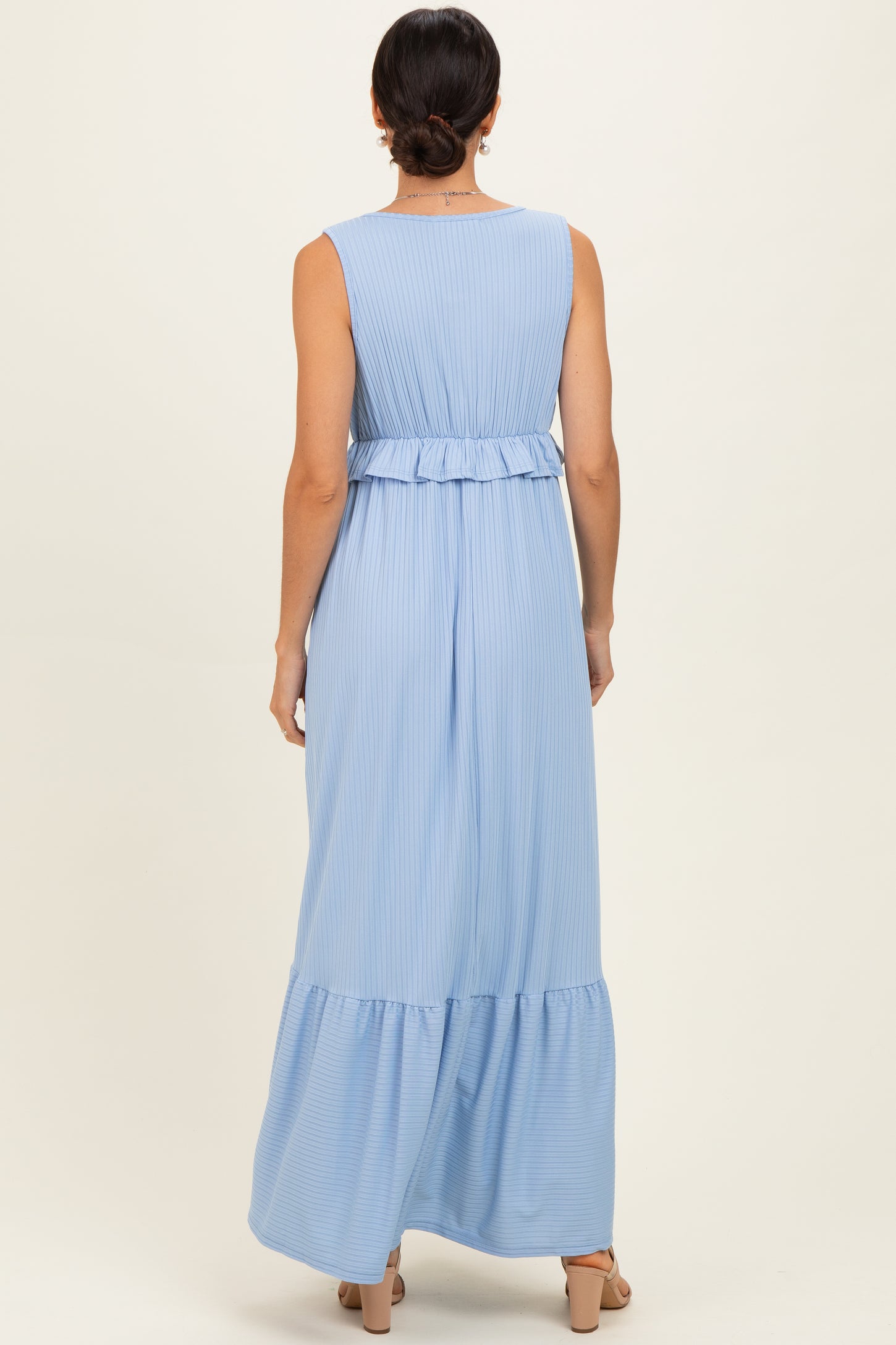 woman wearing a light blue sleeveless maxi dress with a ruffled waist and tiered skirt, viewed from the back