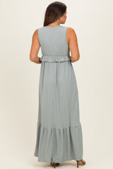 woman wearing a sage green sleeveless maternity maxi dress with a ruffled hem and back pleats