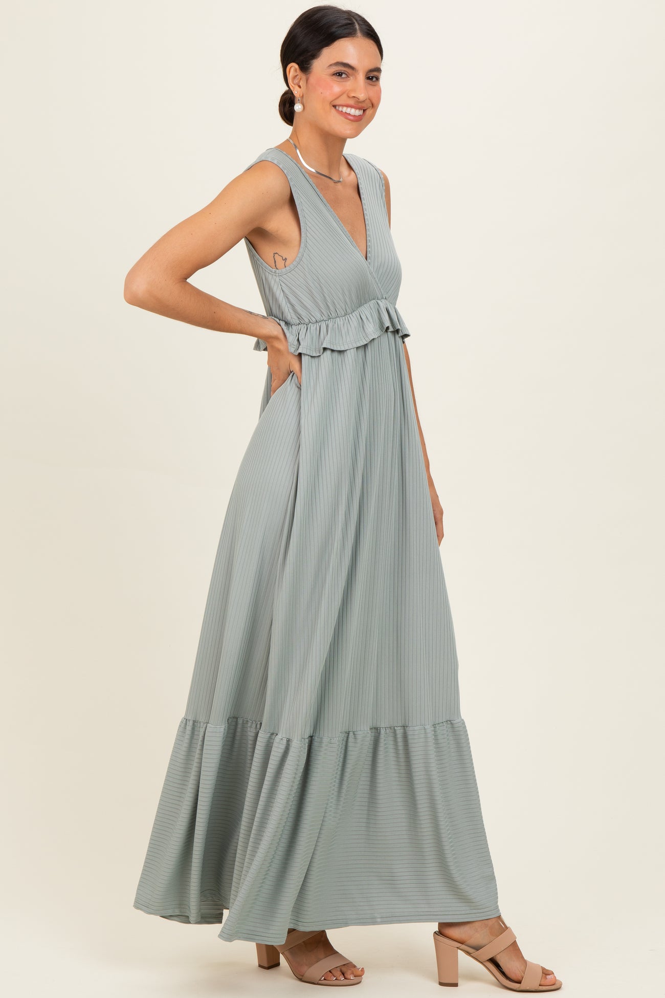 woman wearing a light green striped maxi dress with ruffle details and pockets, smiling and posing sideways
