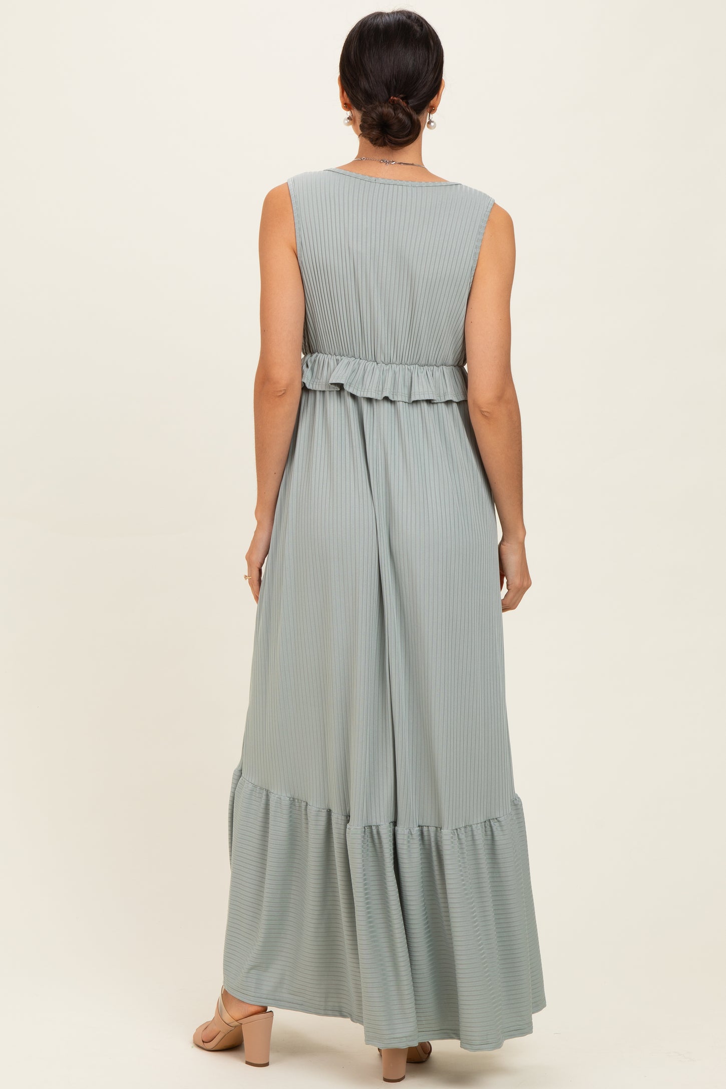 woman wearing a light green sleeveless maxi dress with pleats and a ruffled waist detail, viewed from the back