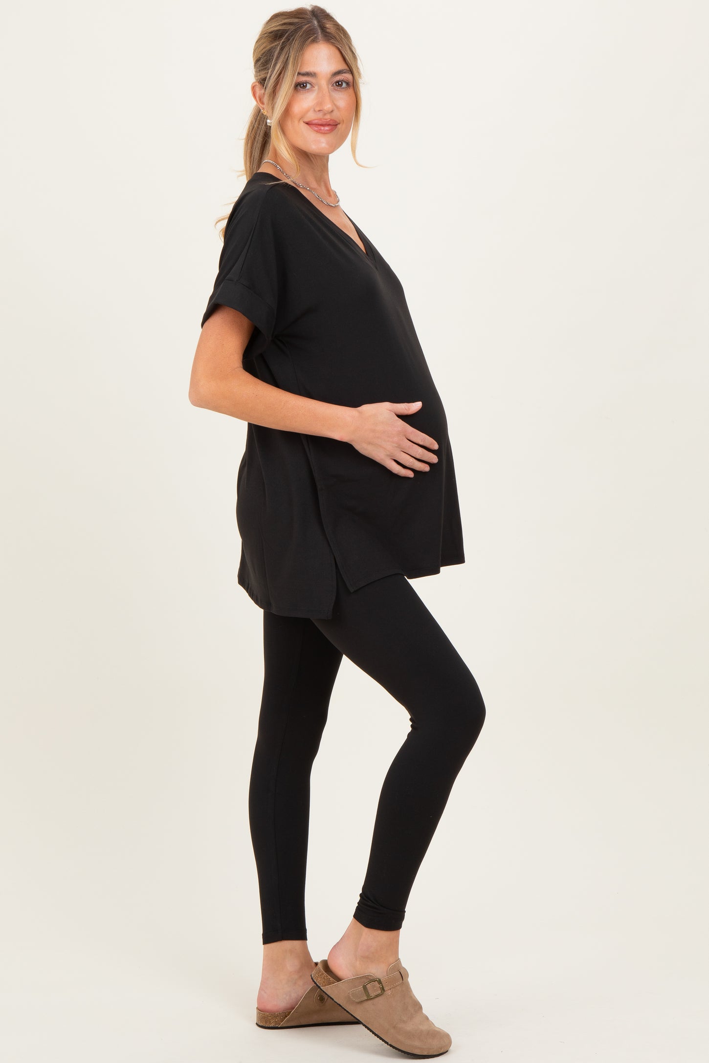woman wearing a black short sleeve maternity top and black leggings, gently cradling her baby bump