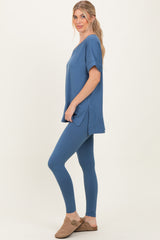 woman wearing a blue oversized top with short sleeves and matching leggings, standing sideways with hands in pockets