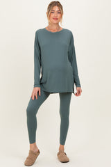 woman wearing a teal long sleeve maternity top and matching leggings, standing with a relaxed pose