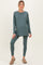 woman wearing a teal long sleeve maternity top and matching leggings, standing with a relaxed pose