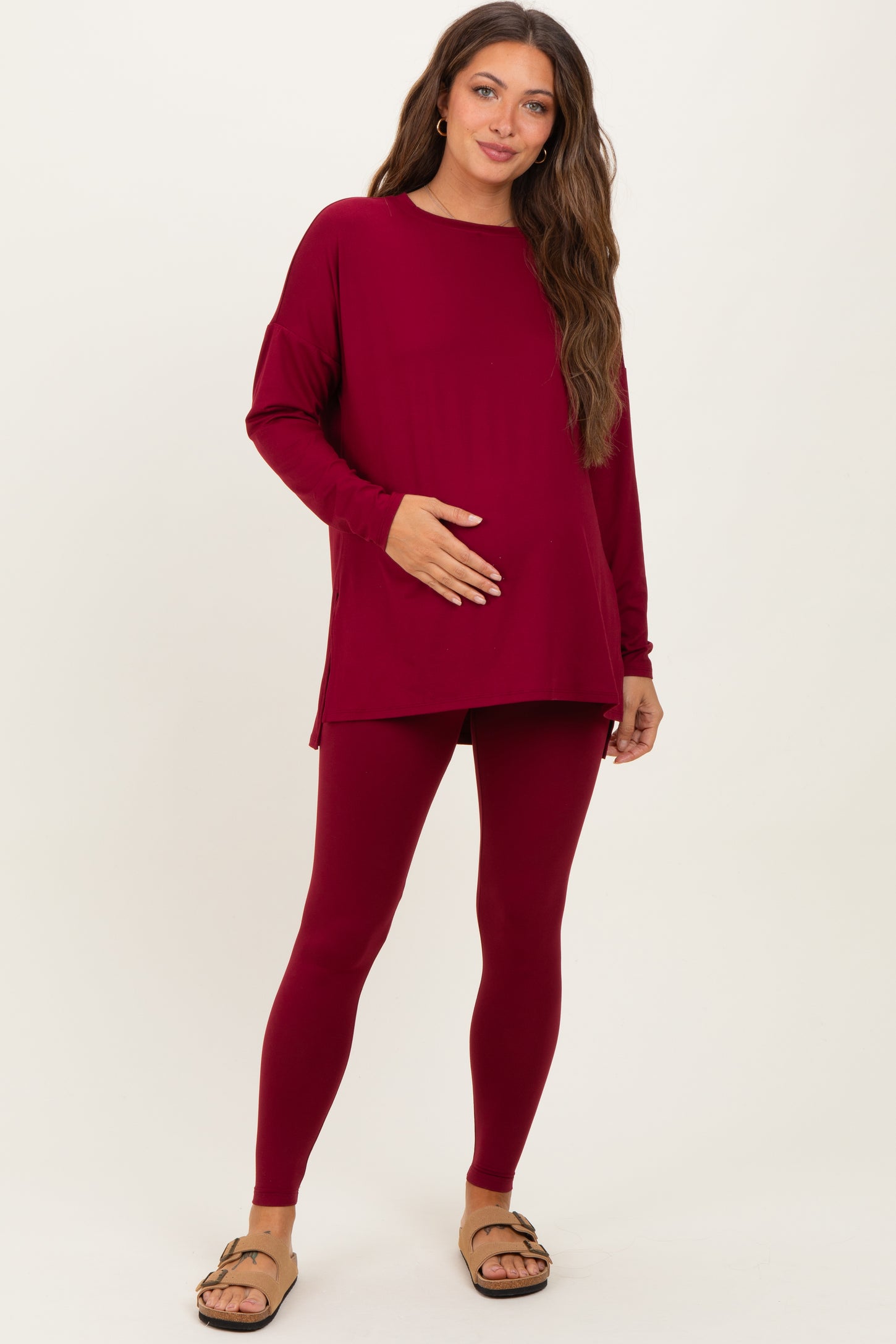 woman wearing a burgundy long sleeve maternity top and matching leggings, holding her baby bump