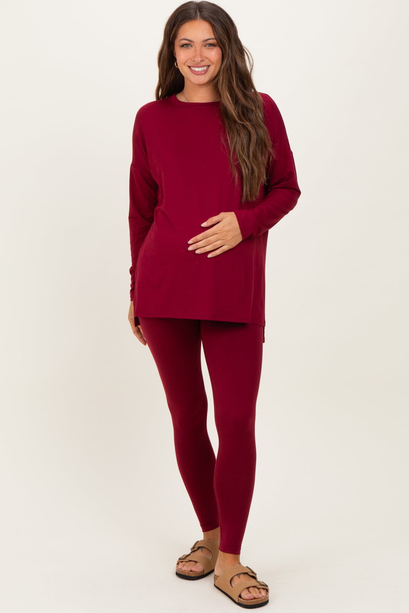 woman wearing a burgundy long sleeve maternity top and matching leggings, holding her baby bump