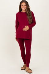 woman wearing a burgundy long sleeve maternity top and matching leggings, holding her baby bump