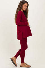 woman wearing a burgundy long sleeve maternity top and matching leggings, holding her baby bump