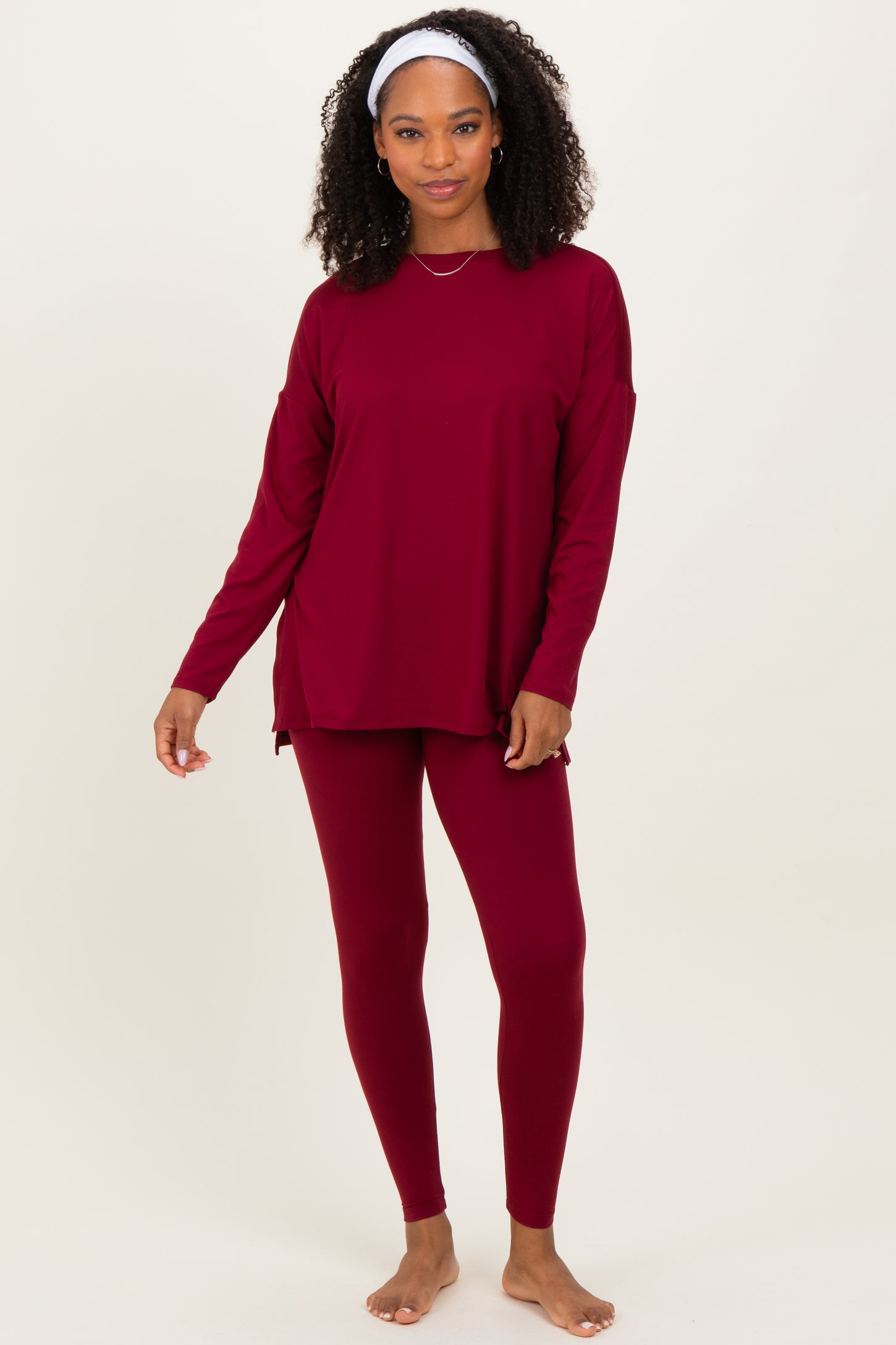 woman wearing a burgundy long sleeve top and matching leggings, standing barefoot with a headband in her hair