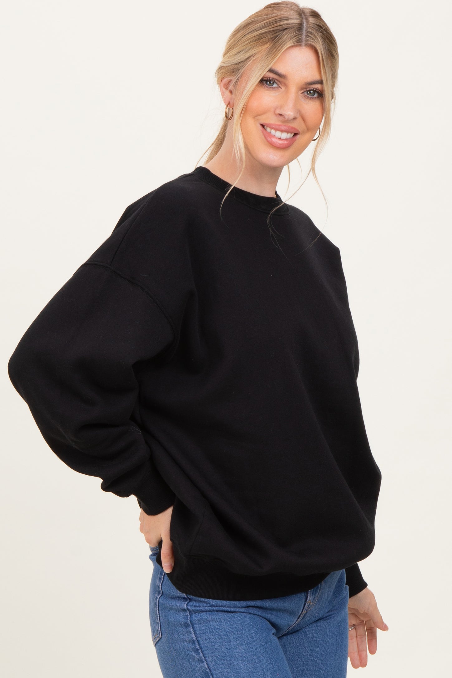 woman wearing a black oversized sweatshirt with long sleeves and a relaxed fit, paired with blue jeans