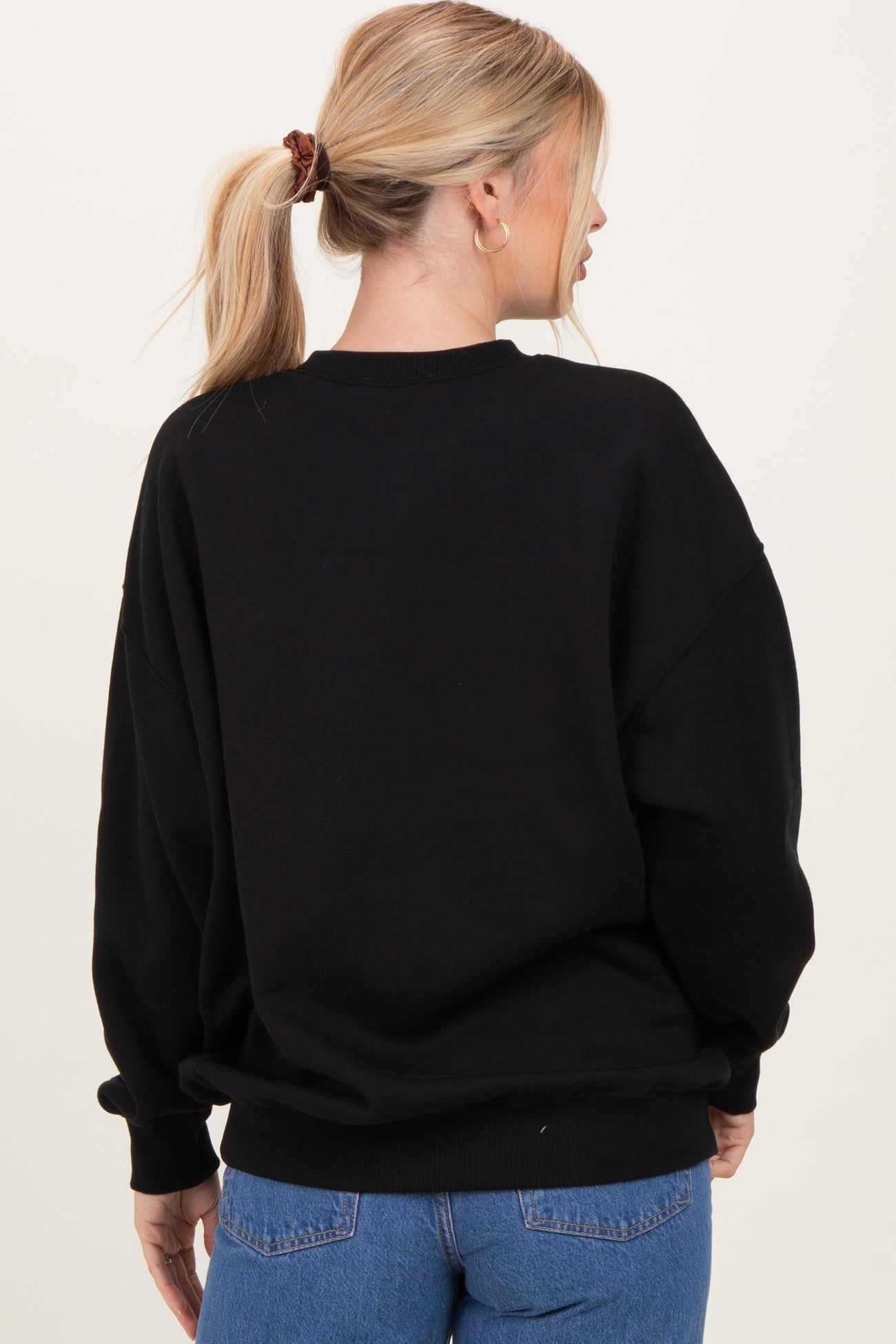 woman wearing a black oversized sweatshirt with dropped shoulders, seen from the back, styled with blue jeans
