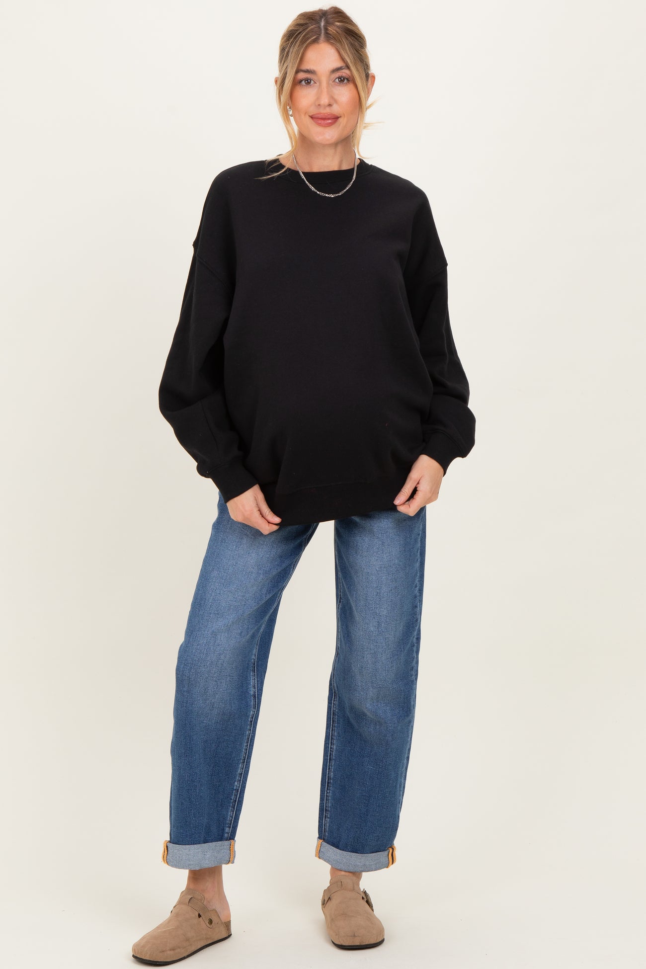 woman wearing a black oversized sweatshirt and blue jeans, showing her baby bump, styled for maternity wear