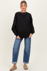 woman wearing a black oversized sweatshirt and blue jeans, showing her baby bump, styled for maternity wear