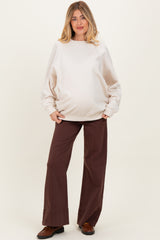 woman wearing a beige maternity sweatshirt and brown wide-leg pants, showcasing her baby bump