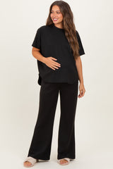 woman wearing a black maternity top and black wide-leg maternity pants, holding her baby bump