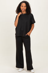 woman wearing a black oversized short sleeve top with wide leg black pants and white sneakers