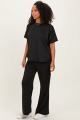 woman wearing a black short sleeve top and black wide leg pants, standing with one hand on her hip