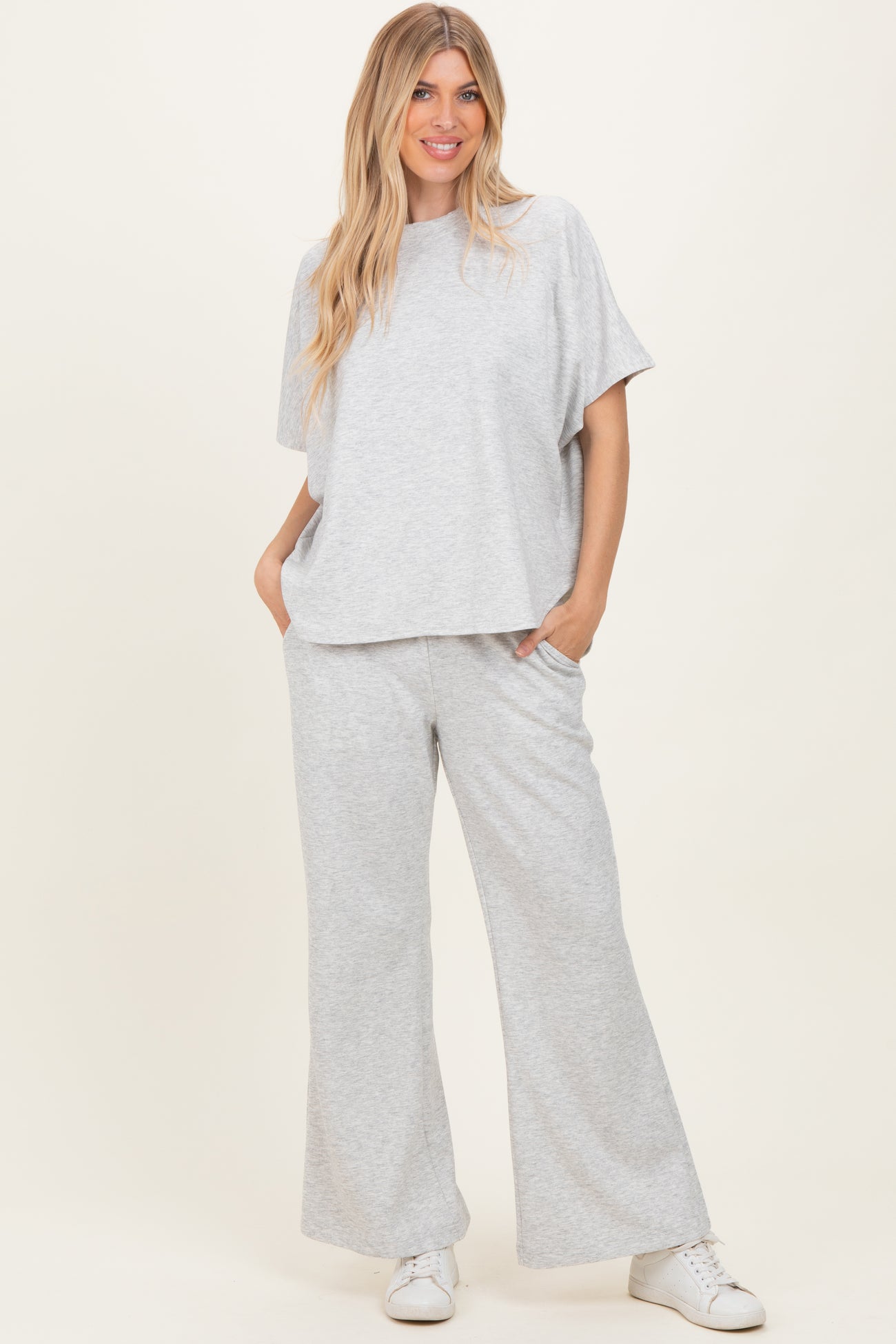 woman wearing a light grey oversized top and matching wide-leg pants, styled casually with white sneakers