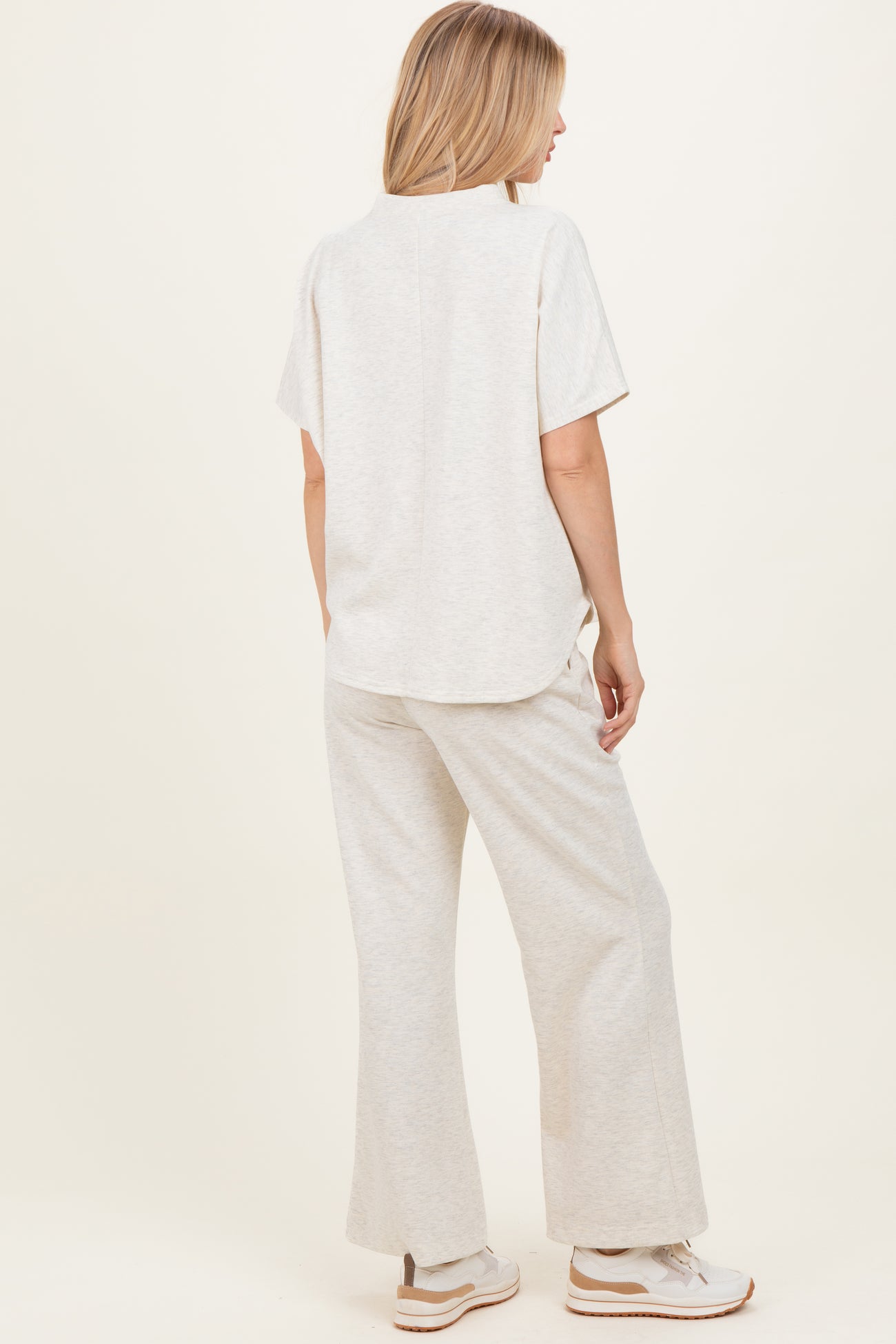 woman wearing a light beige short sleeve top and matching wide-leg pants, standing sideways to show the outfit's fit