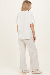 woman wearing a light beige short sleeve top and matching wide-leg pants, standing sideways to show the outfit's fit