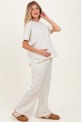 woman wearing a light beige maternity loungewear set with a short sleeve top and wide-leg pants, holding her baby bump