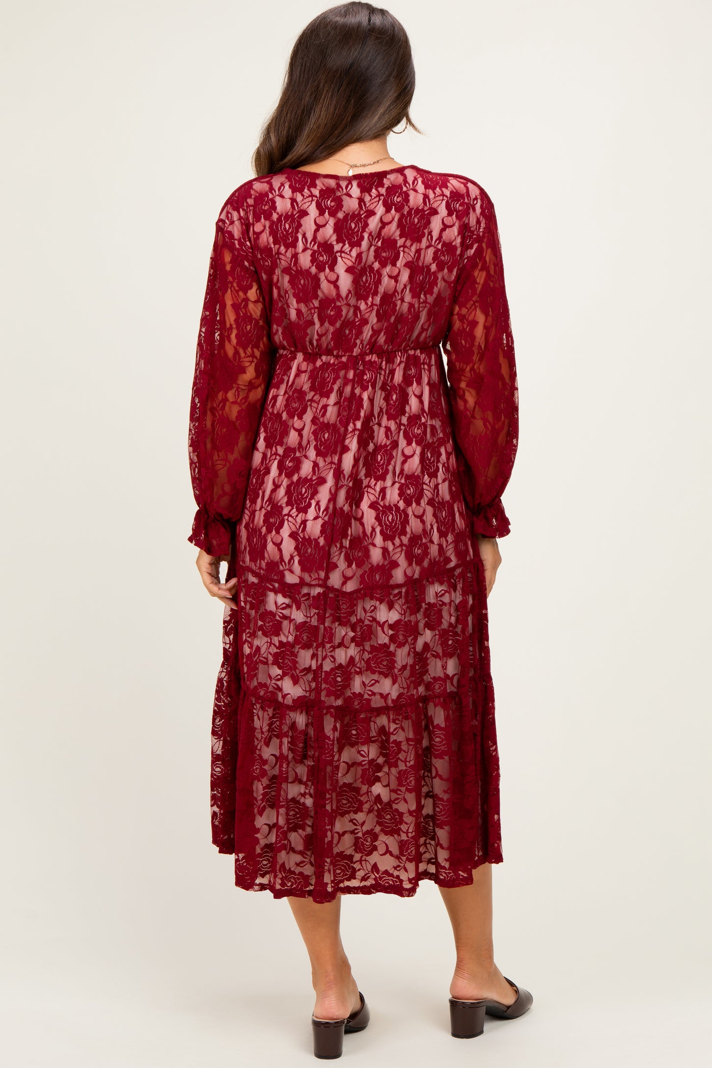 woman wearing a burgundy lace maternity dress with long sleeves and a tiered skirt, showing a flowy silhouette