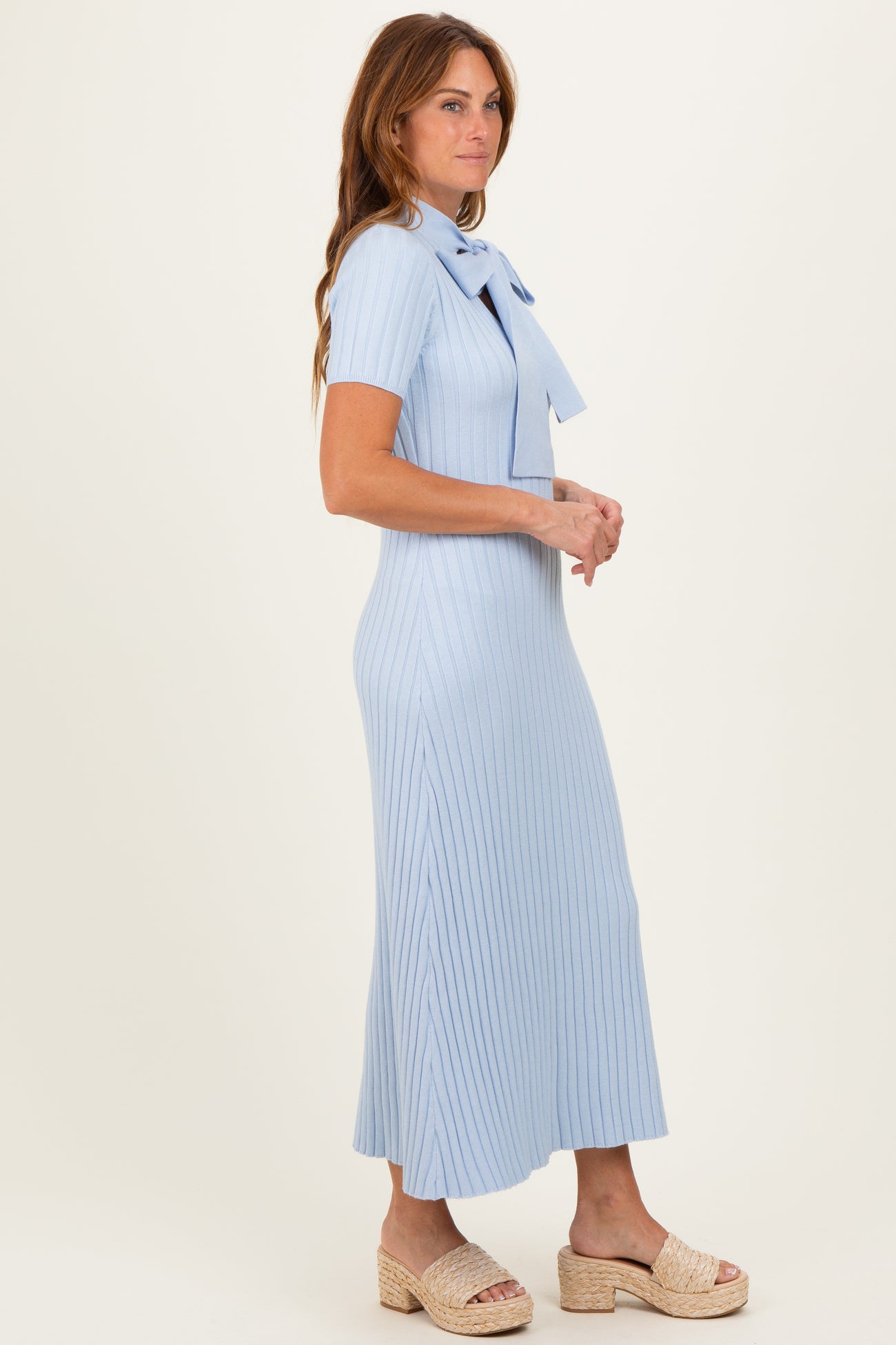 woman wearing a light blue ribbed midi dress with a bow detail at the neckline and a flattering fit
