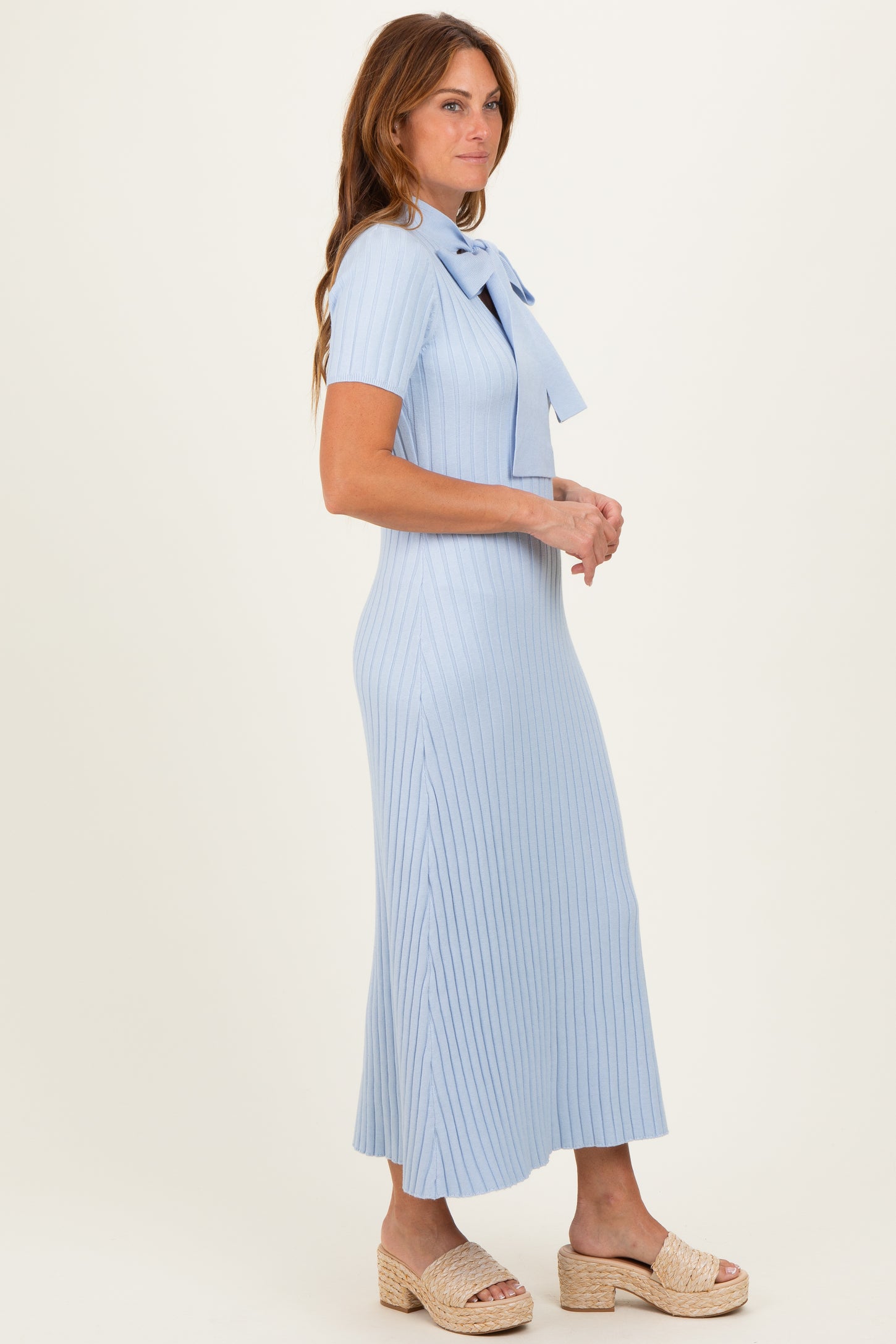 woman wearing a light blue ribbed midi dress with a bow detail at the neckline and a flattering fit