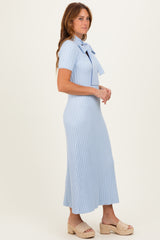woman wearing a light blue ribbed midi dress with a bow detail at the neckline and a flattering fit