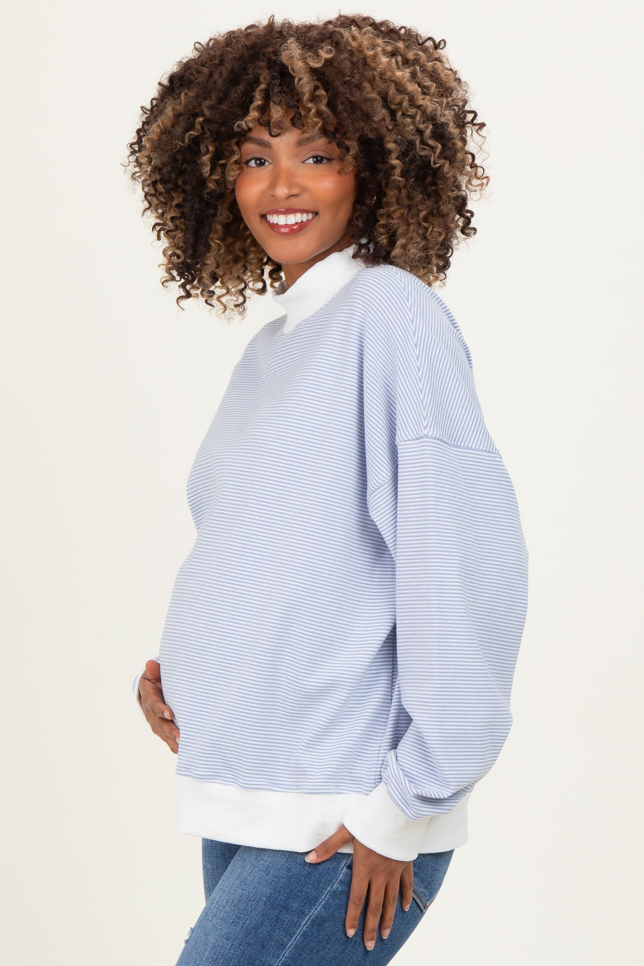 woman wearing a light blue striped maternity pullover with white cuffs and collar, holding her baby bump
