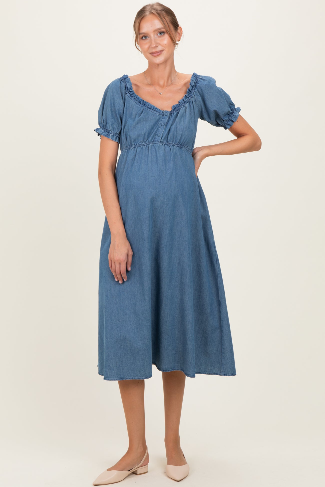 woman wearing a blue denim maternity dress with short ruffled sleeves and a relaxed fit, showcasing her baby bump
