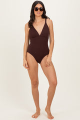 woman wearing a brown ribbed one-piece swimsuit with a deep v-neck and sunglasses