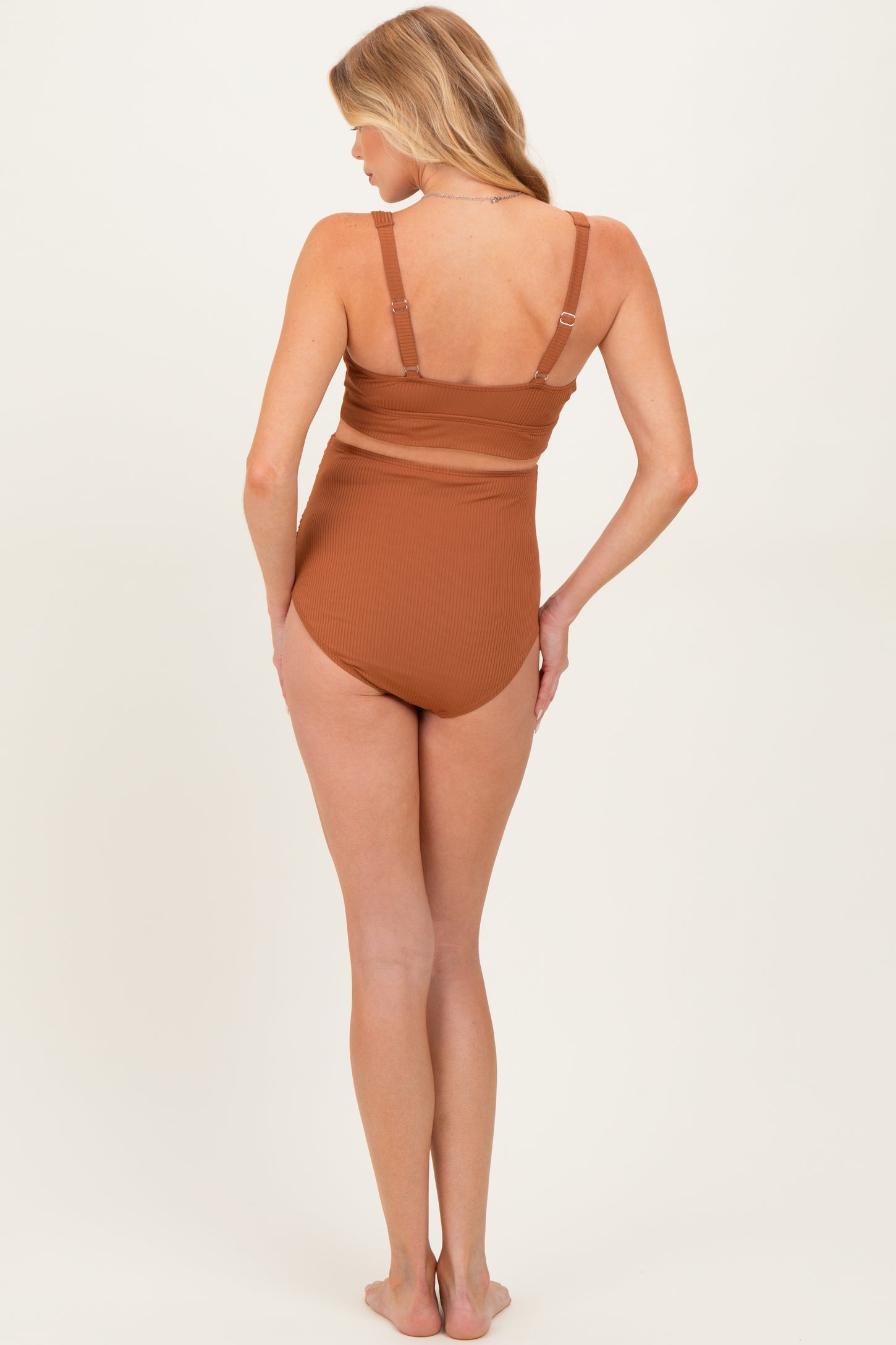 woman wearing a rust brown maternity one-piece swimsuit, showing the back view with adjustable straps
