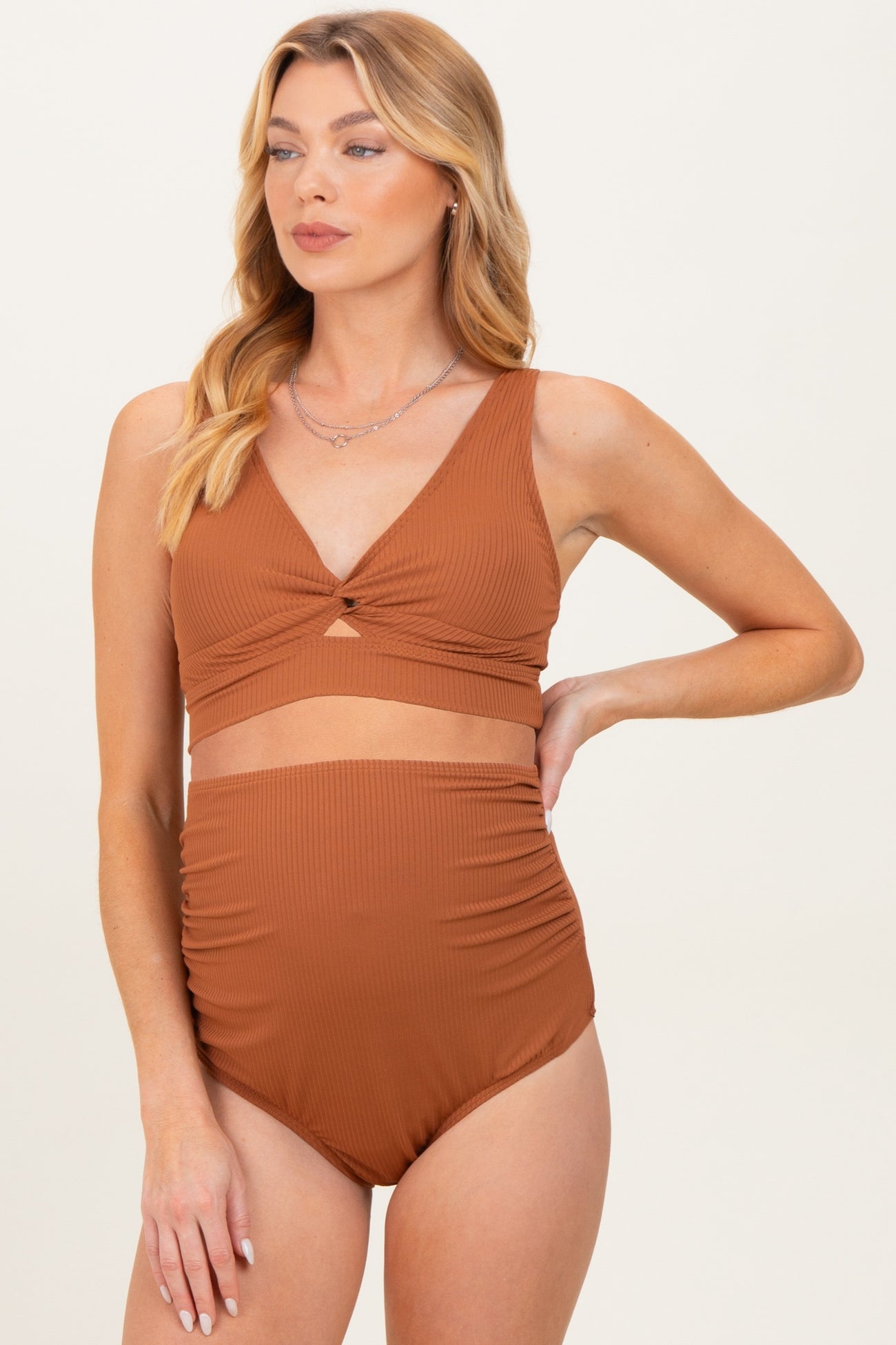 woman wearing a rust-colored maternity bikini top with a twist detail and high-waisted bottom, showing her baby bump