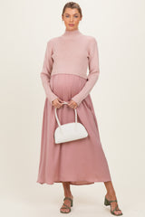 woman wearing a light pink ribbed maternity sweater and a flowy mauve maxi skirt, holding a white handbag and showing her baby bump